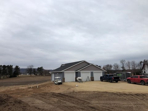 New residential home with two-car garage under construction in rural area with vehicles and bare ground