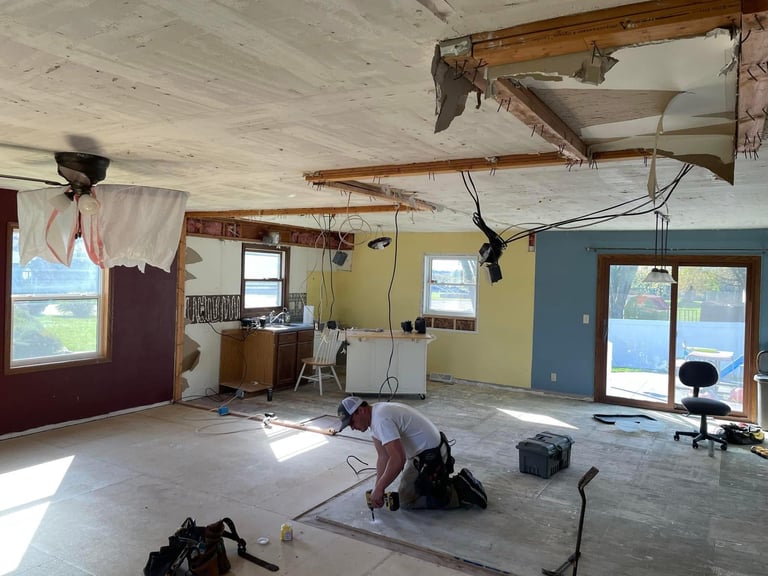 Interior of a renovated space with exposed wooden beams, beige and blue walls, concrete floor, and a person working on construction or renovation