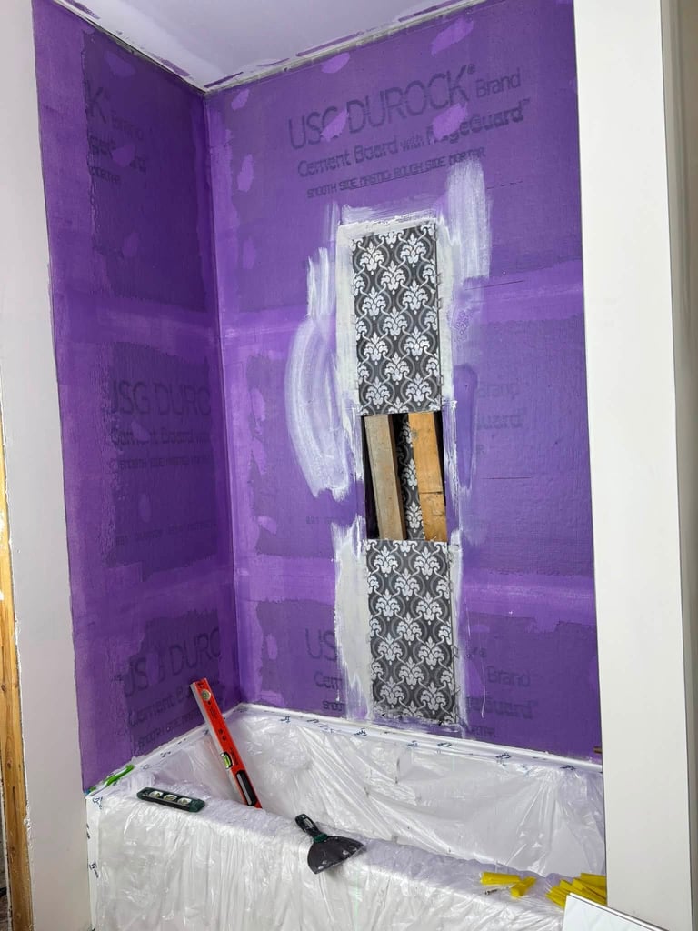 Purple bathroom niche with decorative tile insert under construction, surrounded by plastic sheeting and painting supplies