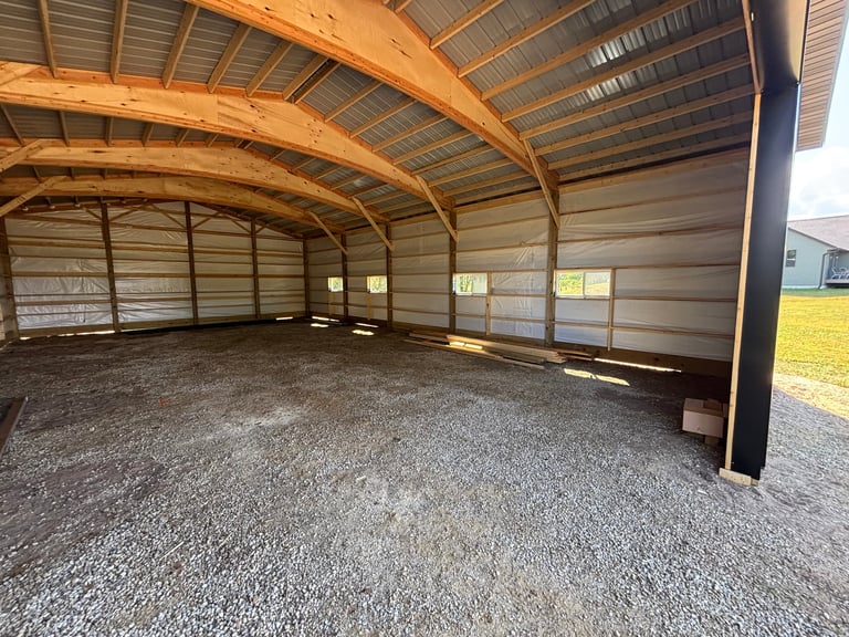 Empty barn interior with wooden beam ceiling, metal walls, and gravel floor