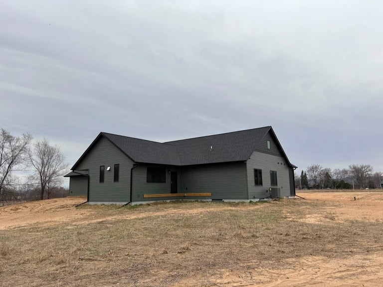 Modern green house with black roof on empty rural land under gray overcast sky