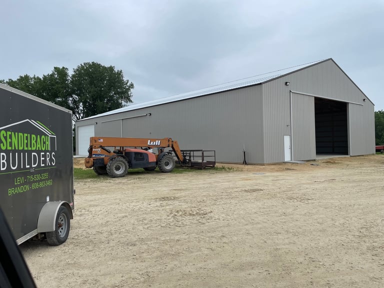 Sendelbach Builders trailer and Skytrak telehandler in front of a large gray metal warehouse under construction on sandy ground