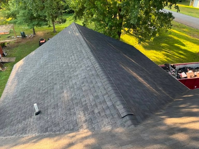 Aerial view of a gray asphalt shingle roof with trees and lawn visible in the background