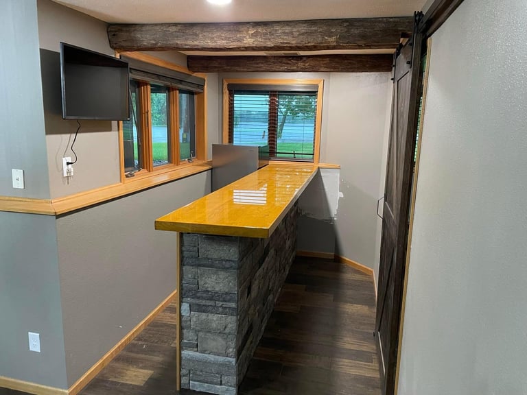 Modern kitchen interior with stone base island, wooden countertop, mounted TV, and large windows overlooking trees