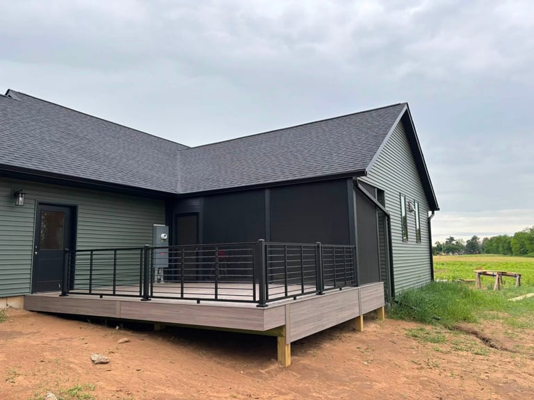 Modern farmhouse with dark exterior and wraparound deck on rural property with open fields
