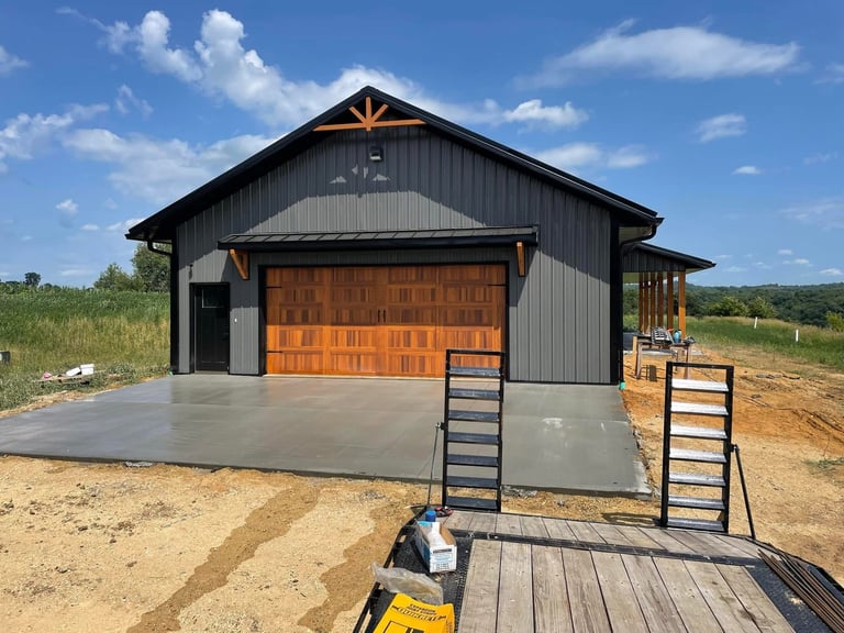 Modern barn building with black metal siding, wood garage door, and concrete foundation on rural property
