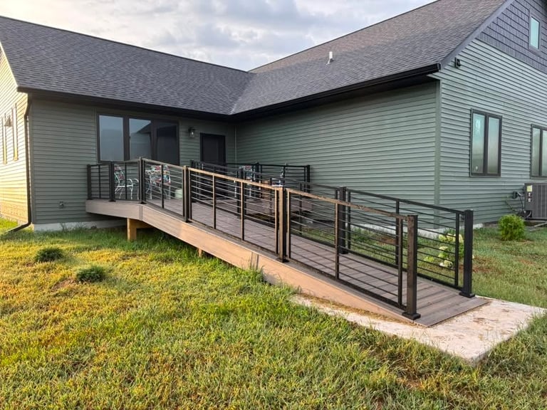 Modern house with gray-green siding and a long wooden deck with black metal railing in a grassy yard
