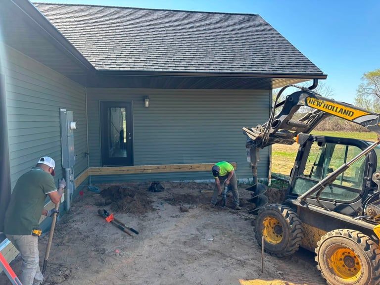 Construction crew working on foundation of new house addition with yellow skid steer loader nearby