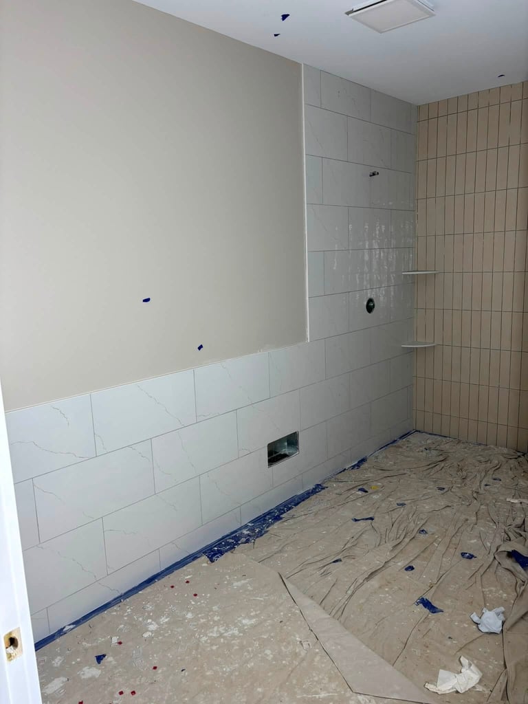 Bathroom under renovation with white subway tiles on walls, concrete floor covered in protective paper, and plumbing fixtures visible during construction.